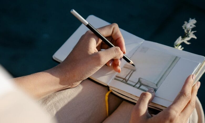 A person drawing with left hand in a notebook
